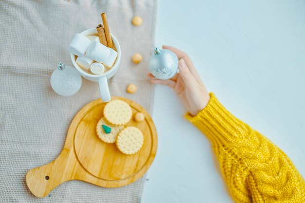 Frau in der gelben Strickjacke, die Weihnachtsball für Dekoration mit Kaffeeeibisch hält