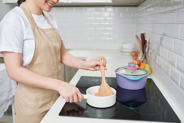 Frau in der Küche mit Holzlöffel kochen. Bio-Frühstück vorbereiten.