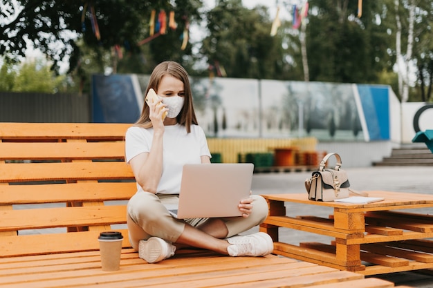 Frau in der medizinischen Gesichtsmaske, die über das Telefon im Freien spricht