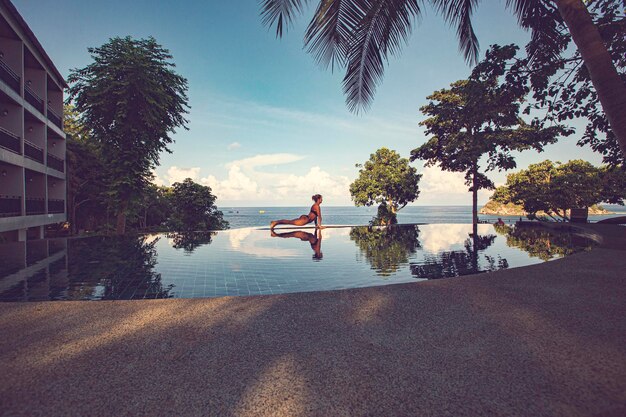 Frau in der Nähe des Swimmingpools beim Yoga, Urdhva mukha svanasana Yoga-Pose, Swimmingpool-Reflexion,