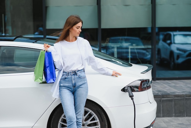 Frau in der Nähe von Elektroauto Fahrzeug an der Ladestation aufgeladen