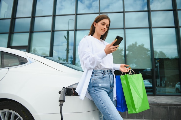 Foto frau in der nähe von elektroauto fahrzeug an der ladestation aufgeladen