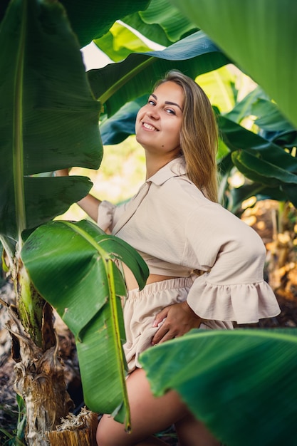 Frau in der Nähe von grünen Blättern von Bananenbüschen in der Natur in einem Park an einem tropischen Ort, sie trägt einen beigen Rock und eine Bluse