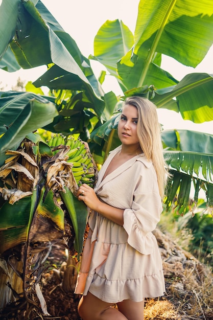 Frau in der Nähe von grünen Blättern von Bananenbüschen in der Natur in einem Park an einem tropischen Ort, sie trägt einen beigen Rock und eine Bluse