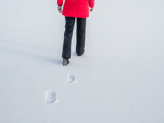 Frau in der roten Jacke, die auf Schnee geht, Fußabdrücke im Schnee, hinterher.