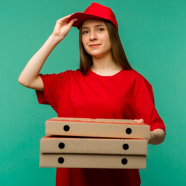 Frau in der roten Kappe, T-Shirt, das Pizzaschachteln der Lebensmittelbestellung auf Blau gibt.