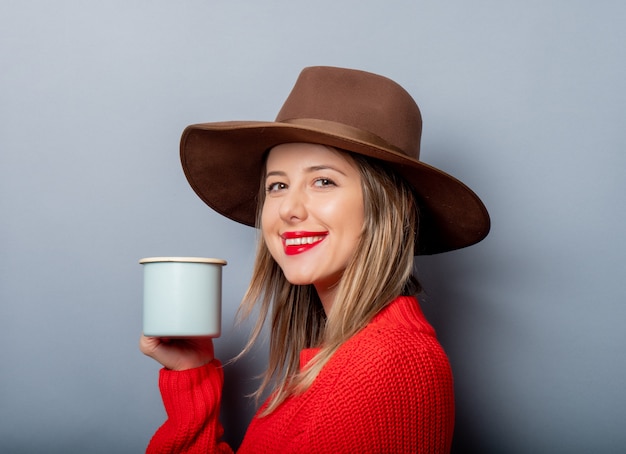 Frau in der roten Strickjacke und im Hut mit Tasse Kaffee
