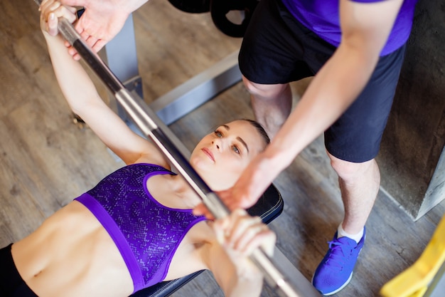 Frau in der Turnhalle mit dem persönlichen Eignungstrainer, der Energiegymnastik mit einem Barbell ausübt.