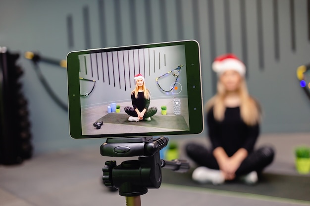 Frau in der Weihnachtsmütze Fitness-Trainer Aufzeichnung Video-Blog mit Kamera auf Stativ.