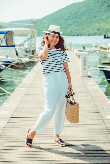 Frau in der weißen Modeluxusansicht, die durch Dockboote auf Hintergrund geht. Sommerzeit