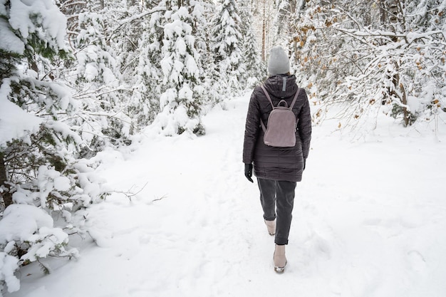 Frau in der Winterjacke, die im verschneiten Winterwald im verschneiten Wintertag spazieren geht
