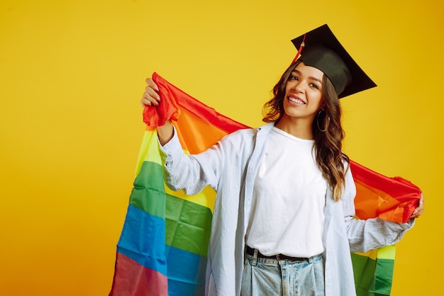 Frau in einem Abschlusshut, der mit LGBT-Regenbogenfahne auf Gelb aufwirft