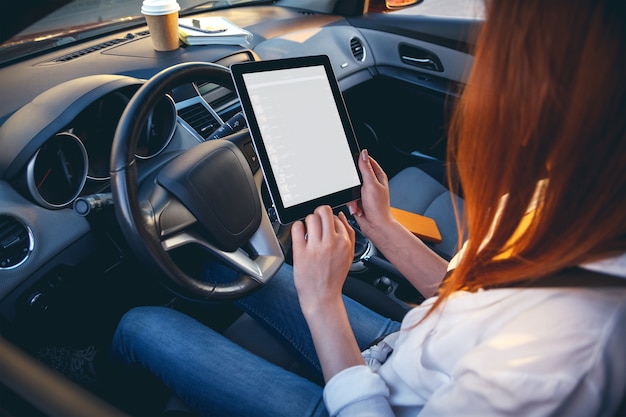 Frau in einem Auto mit einer Tablette in den Händen