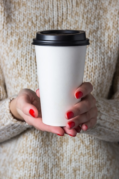 Frau in einem beigen Pullover, der Pappbecher Kaffee hält