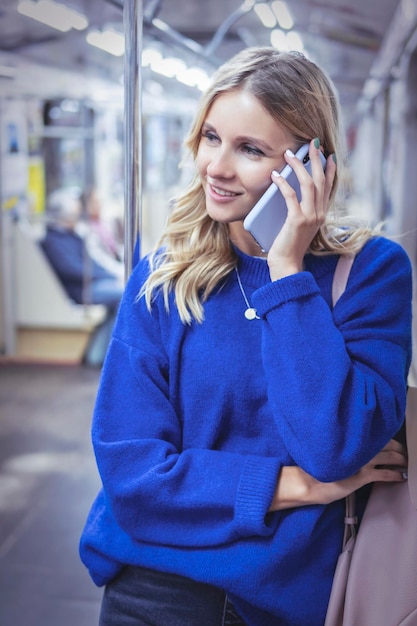 Frau in einem blauen Pullover spricht auf einem Smartphone, während sie in einem U-Bahn-Wagen fährt