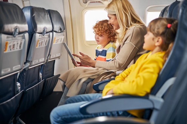 Frau in einem Flugzeug, die einem Jungen ein Tablet zeigt