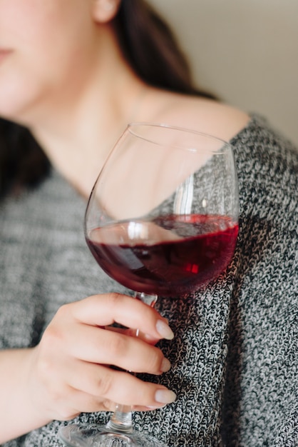 Frau in einem grauen Pullover mit einem Glas Rotwein