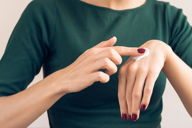 Frau in einem grünen t-shirt und in einer kastanienbraunen maniküre, die handcreme aufträgt