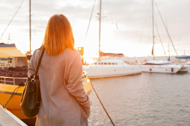 Frau in einem Herbstmantel posiert bei Sonnenaufgang in einem Yachtclub