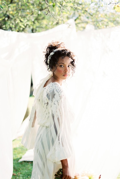Frau in einem Kleid steht nahe den weißen Vorhängen im Garten
