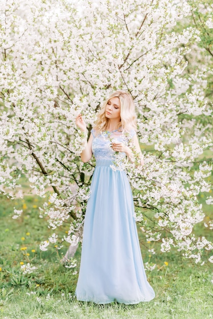 Frau in einem langen blauen Kleid in einem Frühlingsgarten. Zartes Foto mit weißen Blumen