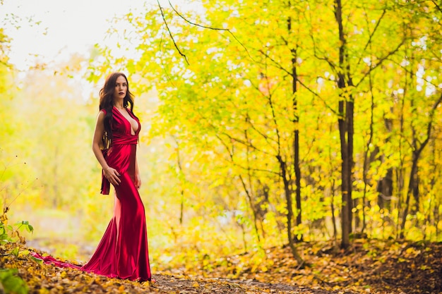 Frau in einem langen roten Kleid allein im Wald. Fabelhaftes und geheimnisvolles Bild eines Mädchens in einem dunklen Wald in der Abendsonne. Sonnenuntergang, Prinzessin ging verloren.