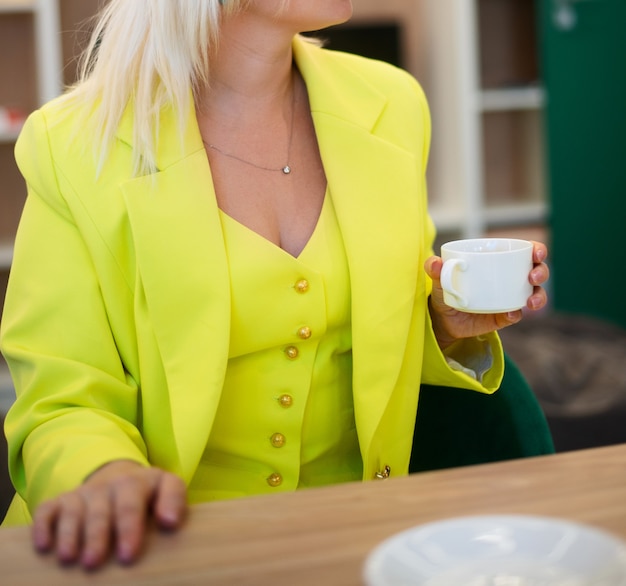 Frau in einem leuchtend gelben Business-Anzug an einem Tisch in einem Sommercafé, nicht wiederzuerkennen