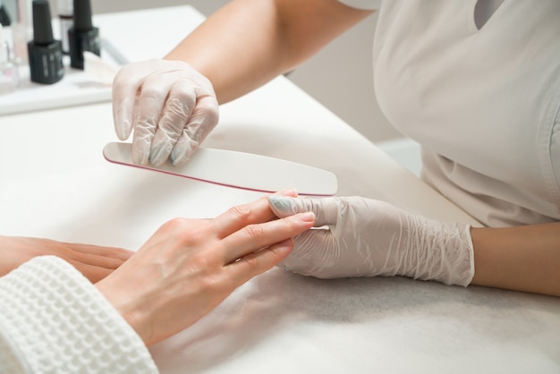 Frau in einem Nagelstudio, die eine Maniküre von einer Kosmetikerin mit Nagelfeileschönheit und Handpflege erhält