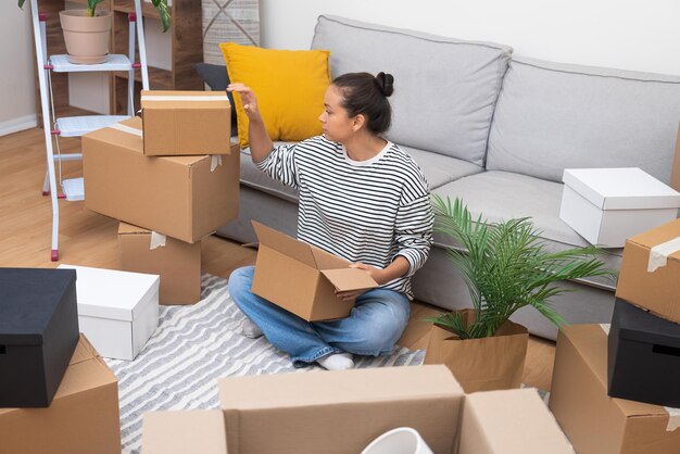 Frau in einem neuen Zuhause inmitten von Kartonboxen, die Optionen für Umzug, Miete, Hauskauf darstellen