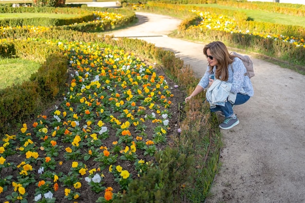 Frau in einem öffentlichen Park mit schönen Blumenbeeten, die die üppige Vegetation betrachten