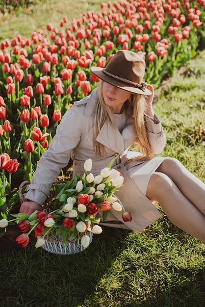 Frau in einem Regenmantel bei Sonnenaufgang zwischen den Reihen der Tulpen