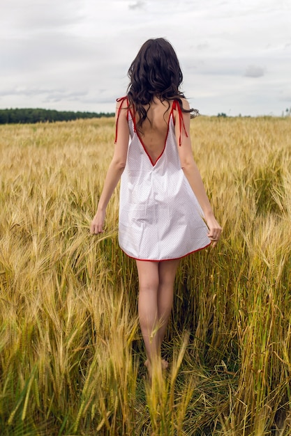 Frau in einem Rotlichtkleid steht im Sommer auf einem Feld mit gelben trockenen Weizenähren
