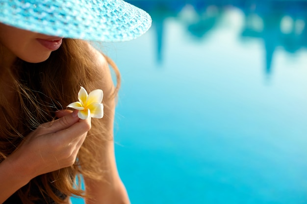 Frau in einem Strohhut, der sich auf einem Liegestuhl nahe einem luxuriösen Sommerpool im Hotel entspannt, Konzeptzeit zu reisen