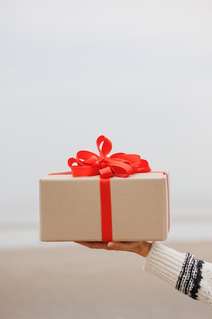 Frau in einem Weihnachtsmann-Hut mit einer Geschenkbox in ihren Händen lächelt eine glückliche Europäerin trägt ein Geschenk für Neujahr oder Weihnachten
