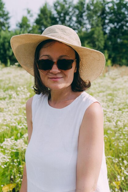 Frau in einem weißen Kleid in der Nähe eines blühenden Feldes mit Gänseblümchen-Strauß Porträt einer Frau von 48 Jahren