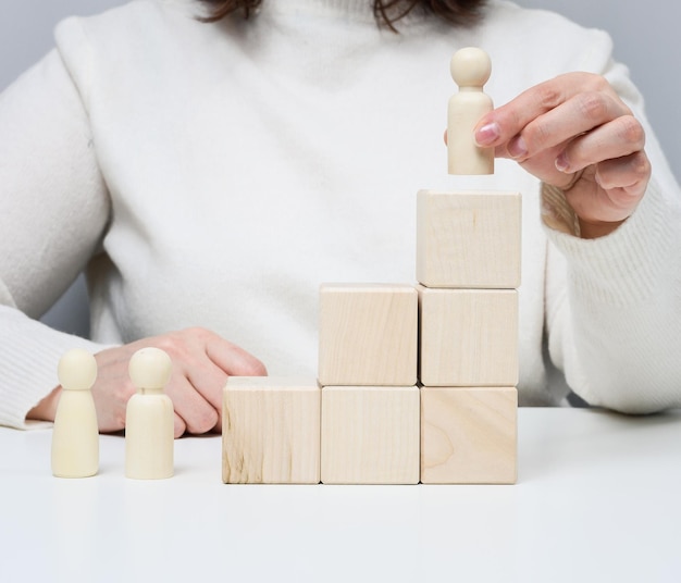 Frau in einem weißen Pullover stellt eine Holzfigur auf das Podium. Das Konzept der Mitarbeitersuche, Karriereförderung. Talentierter Mitarbeiter