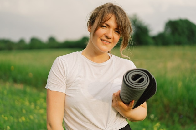 Frau in einem weißen T-Shirt und Leggings macht Yoga auf einem schönen Feld auf einem Sportmatten-Lifestyle