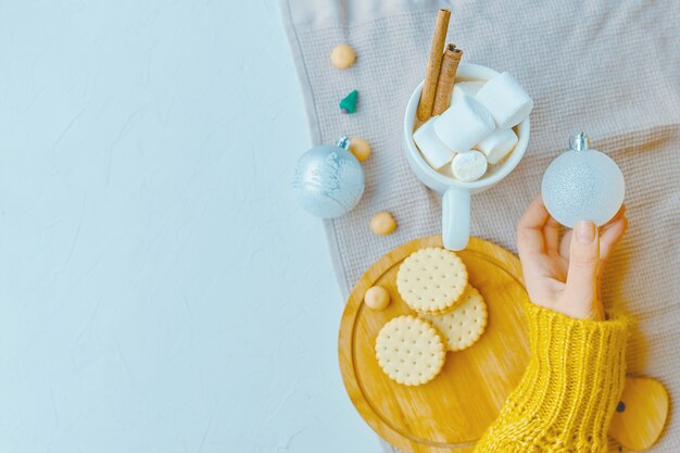 Frau in einer gelben Strickjacke, die ein Weihnachtsspielzeug mit Kakao, Eibisch, Plätzchen hält