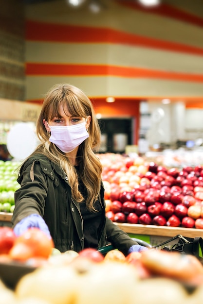 Frau in einer Gesichtsmaske mit Latexhandschuhen beim Einkaufen in einem Supermarkt während der Coronavirus-Quarantäne