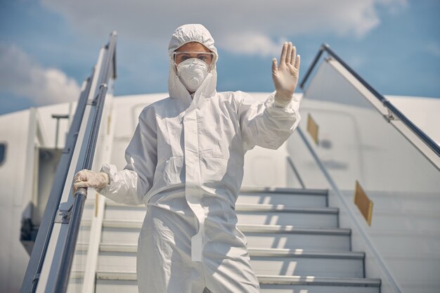 Frau in einer Gesichtsmaske und Einweg-Latexhandschuhen, die mit einer Hand ein Stoppschild zeigen