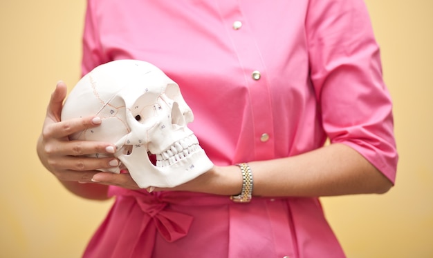 Frau in einer rosa medizinischen Uniform, die einen Schädel in den Händen hält. Anthropologie, Bildung, Wissenschaft, Anatomiekonzept.