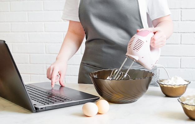 Frau in einer Schürze bereitet Essen zu und sucht im Internet nach einem Rezept. Online-Kochtraining.