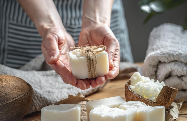 Frau in einer Schürze hält ein Stück weiße handgemachte Kokosseife in ihren Händen Konzept der Herstellung und Verwendung von Naturseife und umweltfreundlicher Kosmetik ein interessantes kreatives Hobby