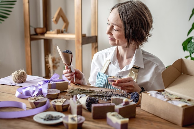 Frau in einer Schürze verpackt natürliche Lavendelseife und dekoriert sie mit Lavendelblüten Konzept von natürlicher Seife und handgefertigten Geschenken