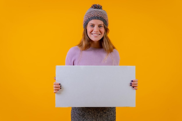 Frau in einer Wollmütze, die auf ein Schild auf einer Anzeige mit gelbem Hintergrund zeigt