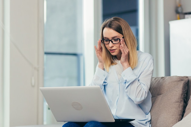 Frau in Freizeitkleidung, die zu Hause auf einem Sofa sitzt und einen Laptop für die Videokommunikation verwendet