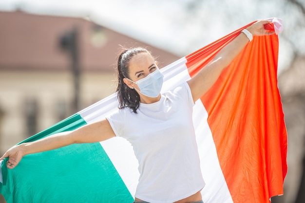 Frau in Gesichtsmaske hält italienische Flagge auf einer Straße, die die Aufhebung der aufgrund eines Coronavirus eingeführten Beschränkungen feiert.