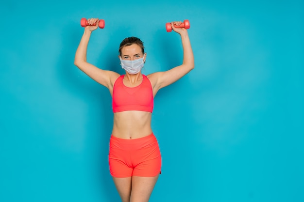 Frau in Gesichtsschutzmaske und Fitnessbekleidung auf blauem Hintergrund isoliert.