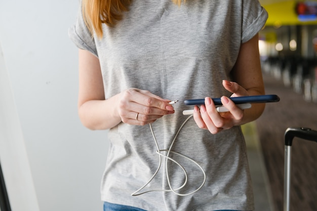 Frau in grauem Hemd steckte USB-Kabel vom tragbaren Ladegerät zum Handy-Akku in der Nähe des Hintergrunds des Flughafenterminals