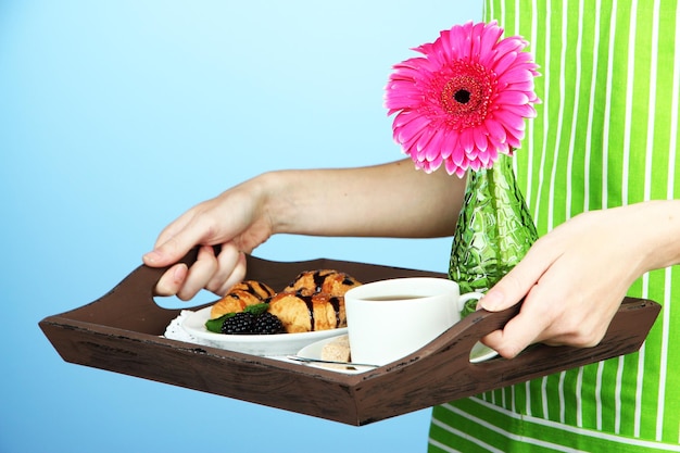 Frau in grüner Schürze mit Holztablett mit Frühstück auf farbigem Hintergrund